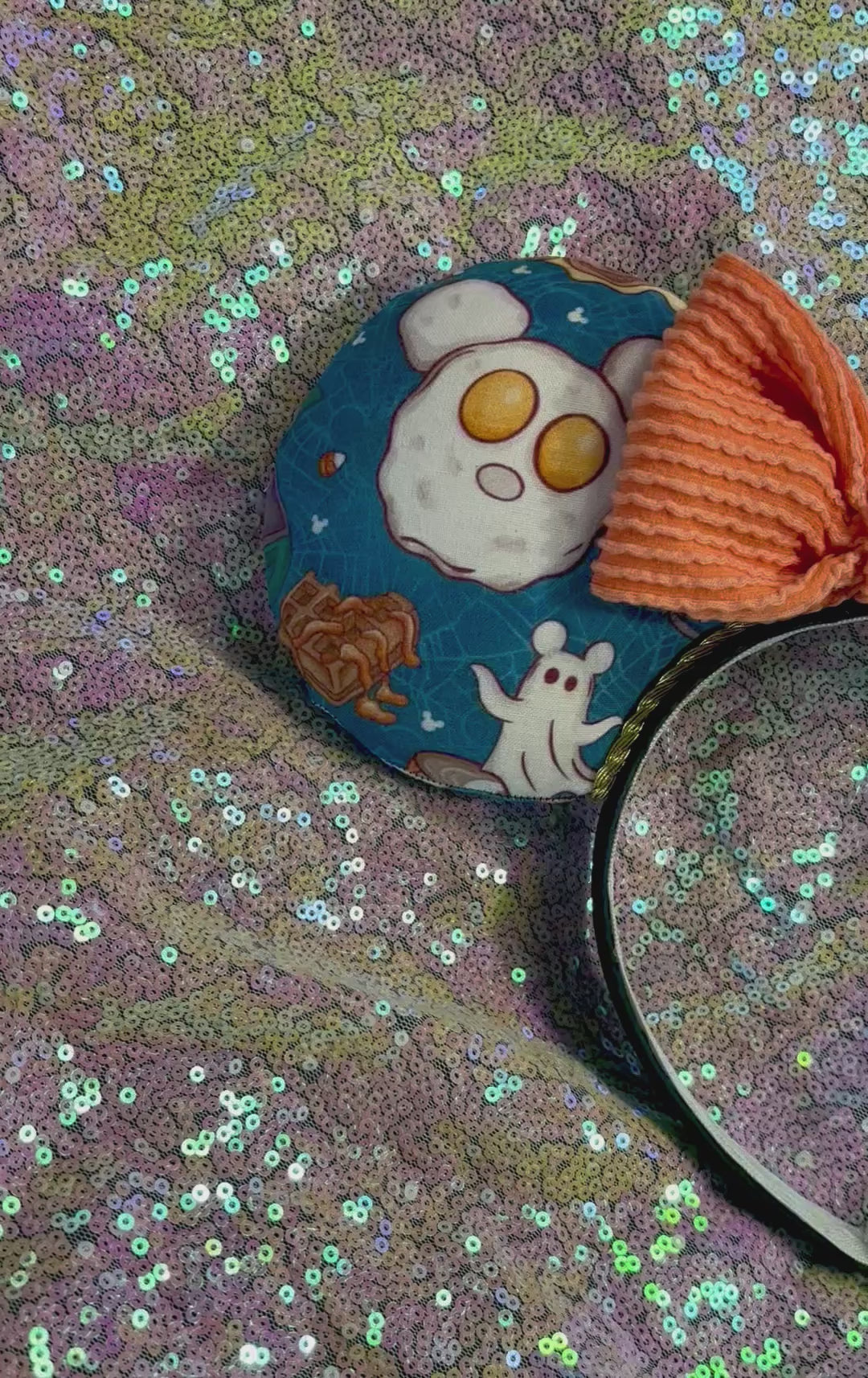 Handmade and ready to ship Fall Mouse ears with pumpkins, eggs, waffles and more shaped like mouse ears is on the front and back of mouse ears with a orange waffle print bow on a rainbow  glitter background.