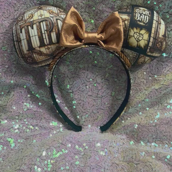 Mouse ear headband in TTPD design with a black sequin bow on a textured gray surface.