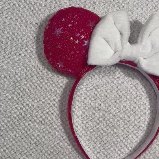 Handmade and ready to ship red mouse ears with iridescent stars on both the front and back along with the headband as well. The set has a white soft bow. Item is shown on a white background.