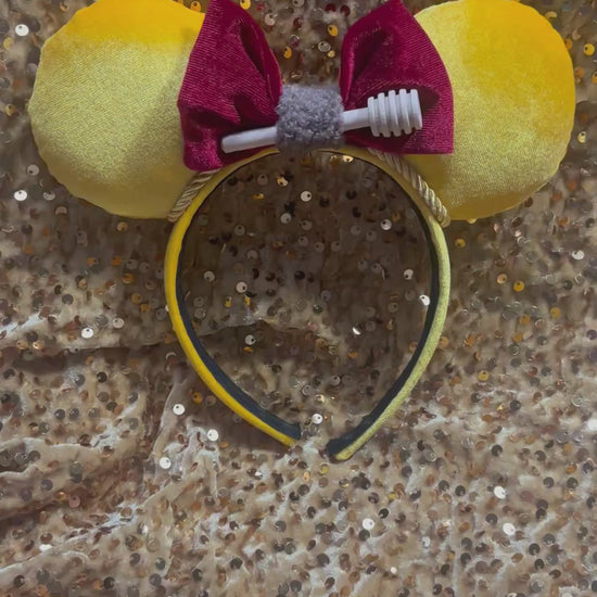 Yellow mouse ears with a red bow with a mini honeycomb and fluffy brown middle on a textured beige surface
