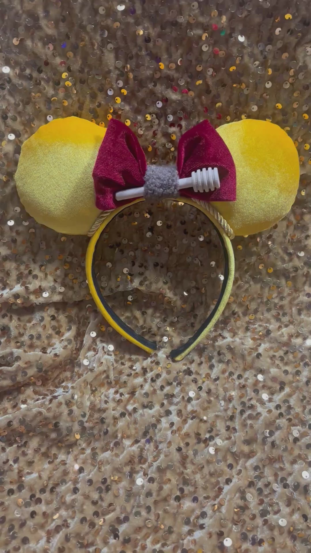 Yellow mouse ears with a red bow with a mini honeycomb and fluffy brown middle on a textured beige surface