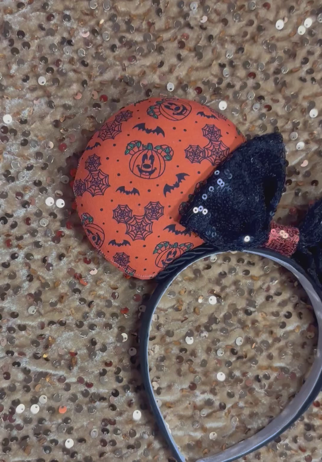 Halloween mouse ears with the fabric on both the front and back. It's orange with bats, mouse shaped pumpkins and spider webs. The headband is black universal sized and fits most. The set has a black with orange middle sequin bow. Item is shown on a gold sequin background.