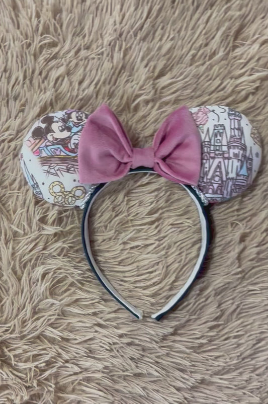 A pair of handmade ear headbands with a large dusty pink velvet bow, featuring printed park themed patterns on the ears.