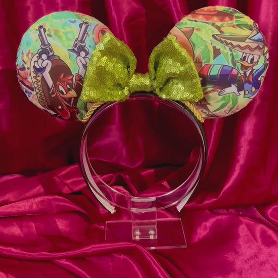 Colorful Handmade mouse ears with a green bow on a red satin background with duck cartoon images on the ears