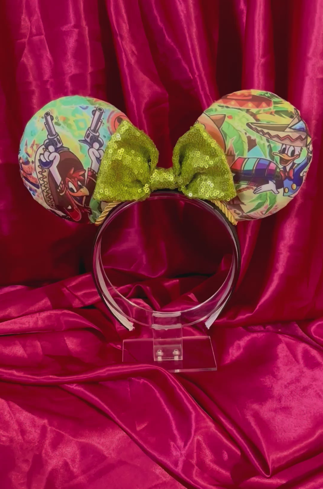 Colorful Handmade mouse ears with a green bow on a red satin background with duck cartoon images on the ears