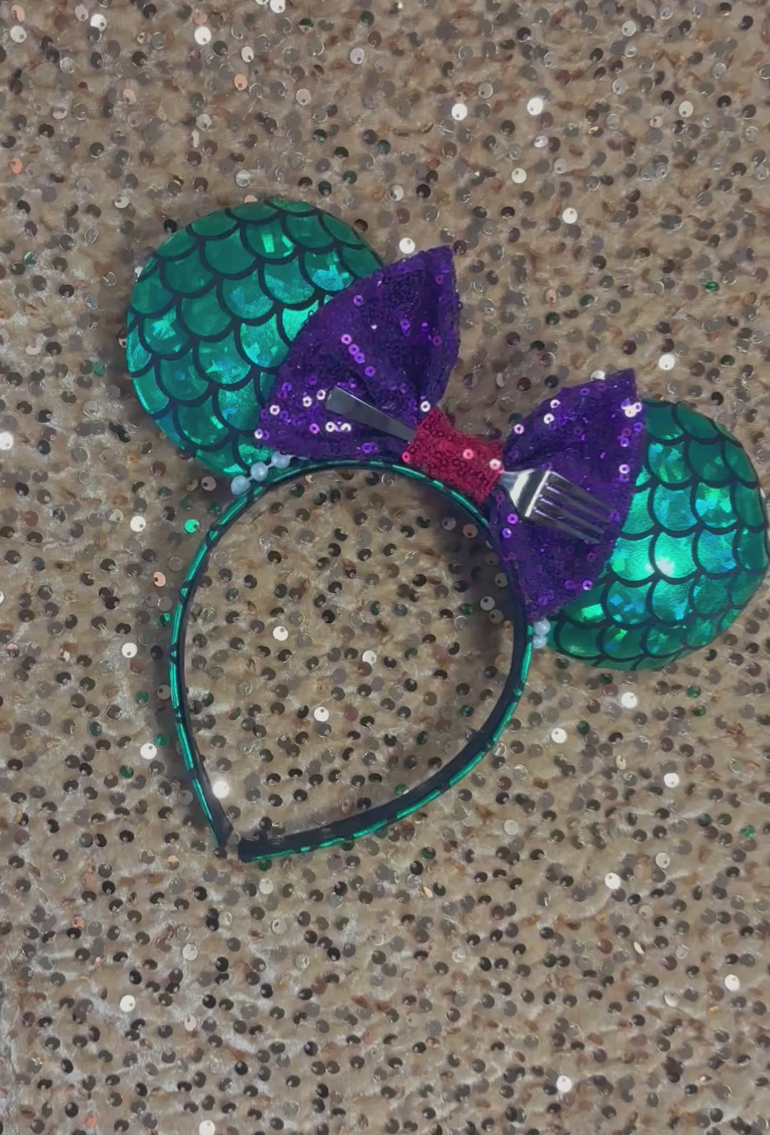 Mermaid-themed headband with teal scales and a purple sequin bow with a red middle and a dinglehopper middle piece. Pearl garland trim along inner ears m on a matching mermaid scales headband.