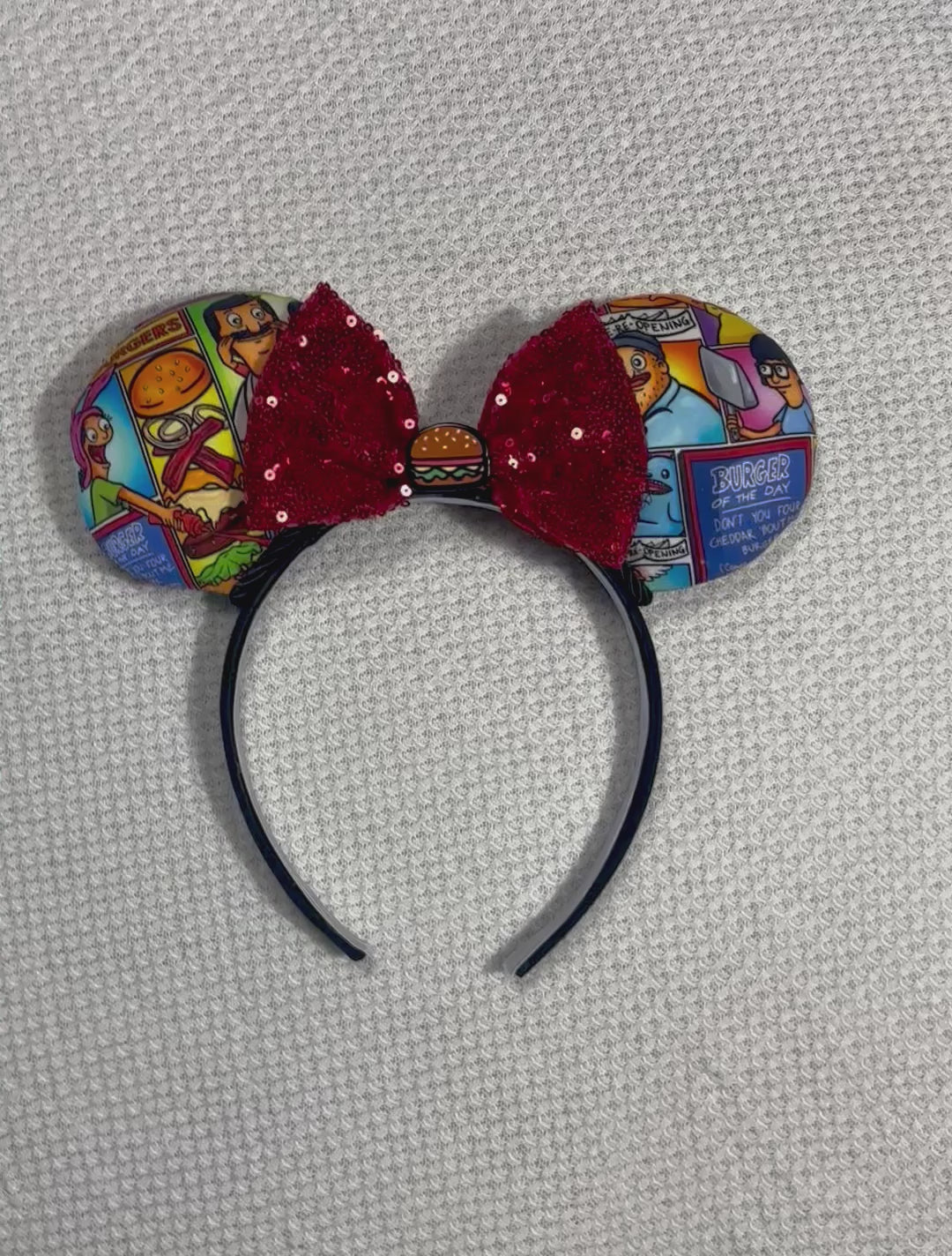 Handmade and ready to ship Belcher and friends mouse ears with the fabric on both the front and back. The headband is black universal sized and fits most. The set has a red sequin bow with a burger embellishment on the middle. Item is shown on a white background.