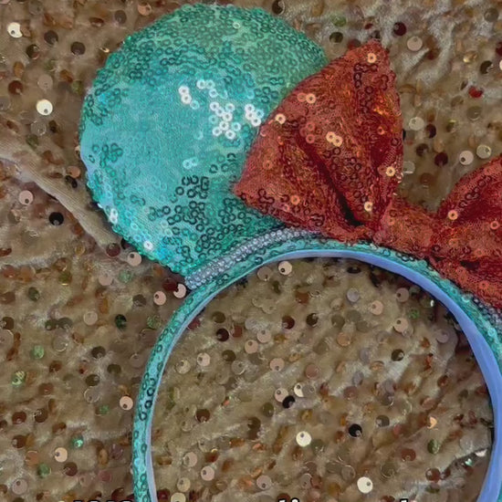 Glittery green and orange mouse ears inspired for the showgirls. Rhinestone trim is on the ears as well. Shown  against a glittery gold background