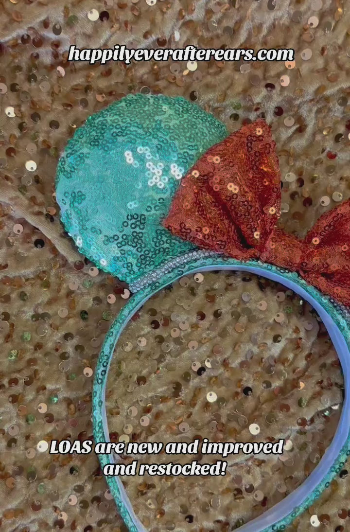 Glittery green and orange mouse ears inspired for the showgirls. Rhinestone trim is on the ears as well. Shown  against a glittery gold background