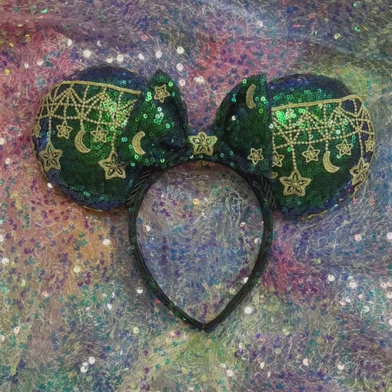 Mouse Ear headband that is a Handmade Iridescent blue and green sequins with gold sun, moon and stars attached to them. bow with star and moon patterns on a glittery background.