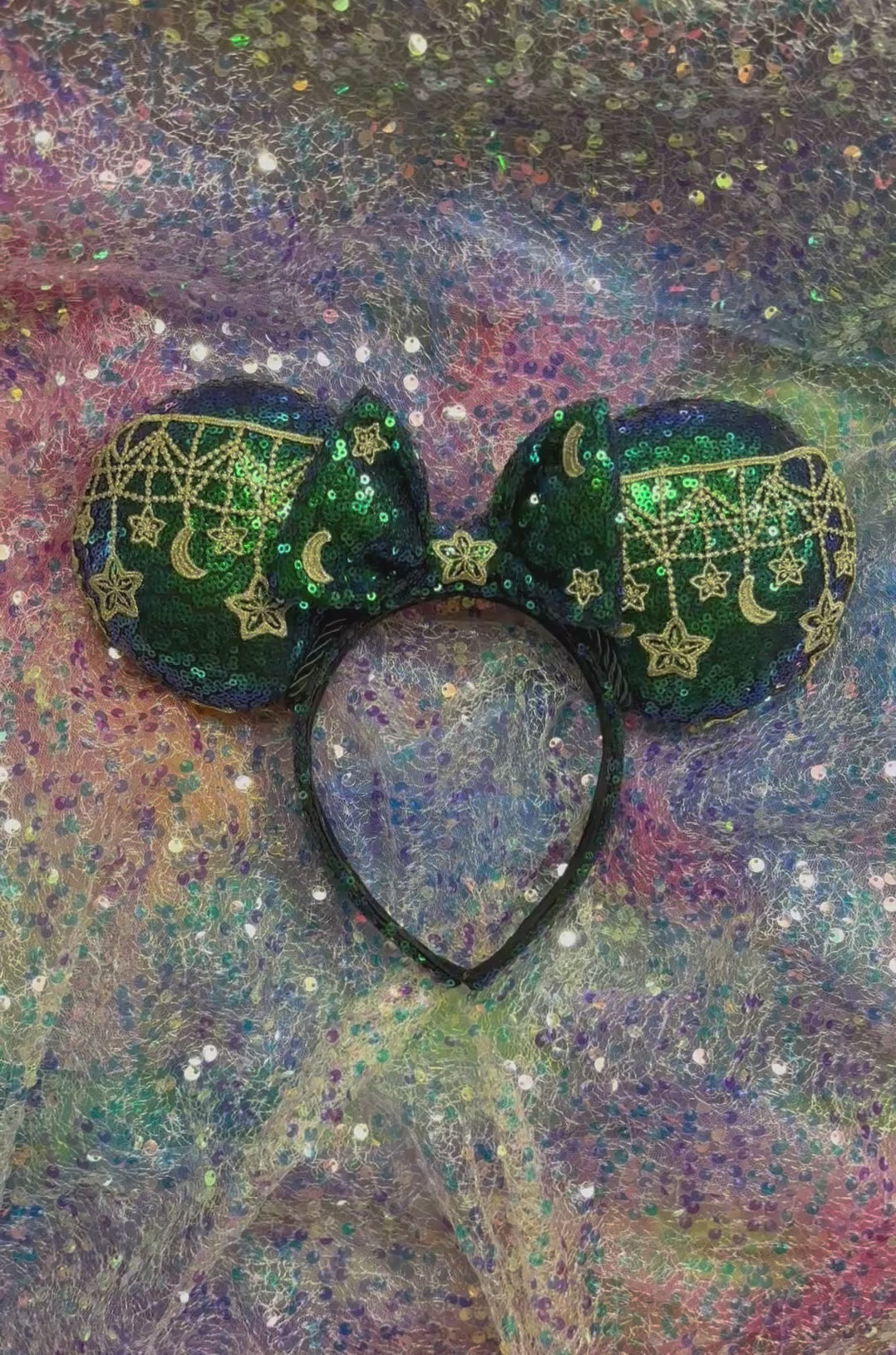 Mouse Ear headband that is a Handmade Iridescent blue and green sequins with gold sun, moon and stars attached to them. bow with star and moon patterns on a glittery background.