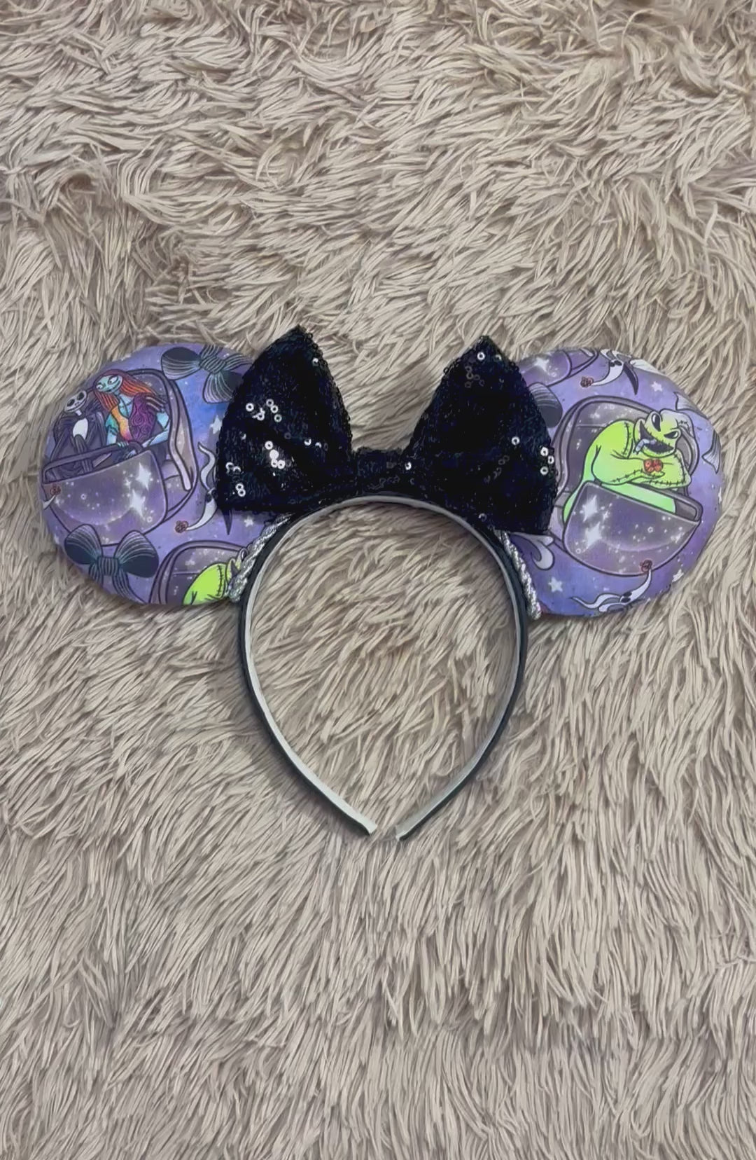 An ear headband accessory with a black sequined bow, featuring a purple HM and NBC themed print with a cartoon character in a buggy.