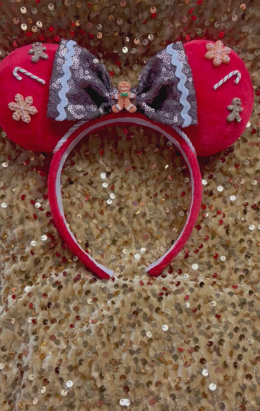 Decorative headband with red ears, black bow, gingerbread men, and candy canes on a gold glitter background