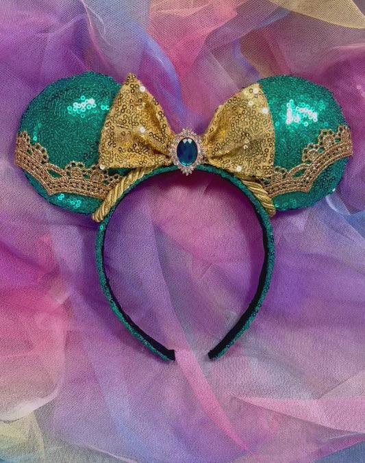 Handmade, and ready to ship. Jasmine inspired Mouse ear headband with teal sequin fabric on the front and back of ears with a gold sequin bow with a teal embellishment in the middle of bow. gold along the ears and the trim as well. Mouse ears are on a Universal sized headband that also has teal on it. 