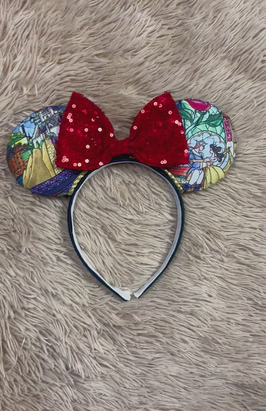A pair of ears headband featuring a vibrant red sequined bow in the center and patterned fabric ears with colorful stained-glass style illustrations, displayed on a beige faux fur background.