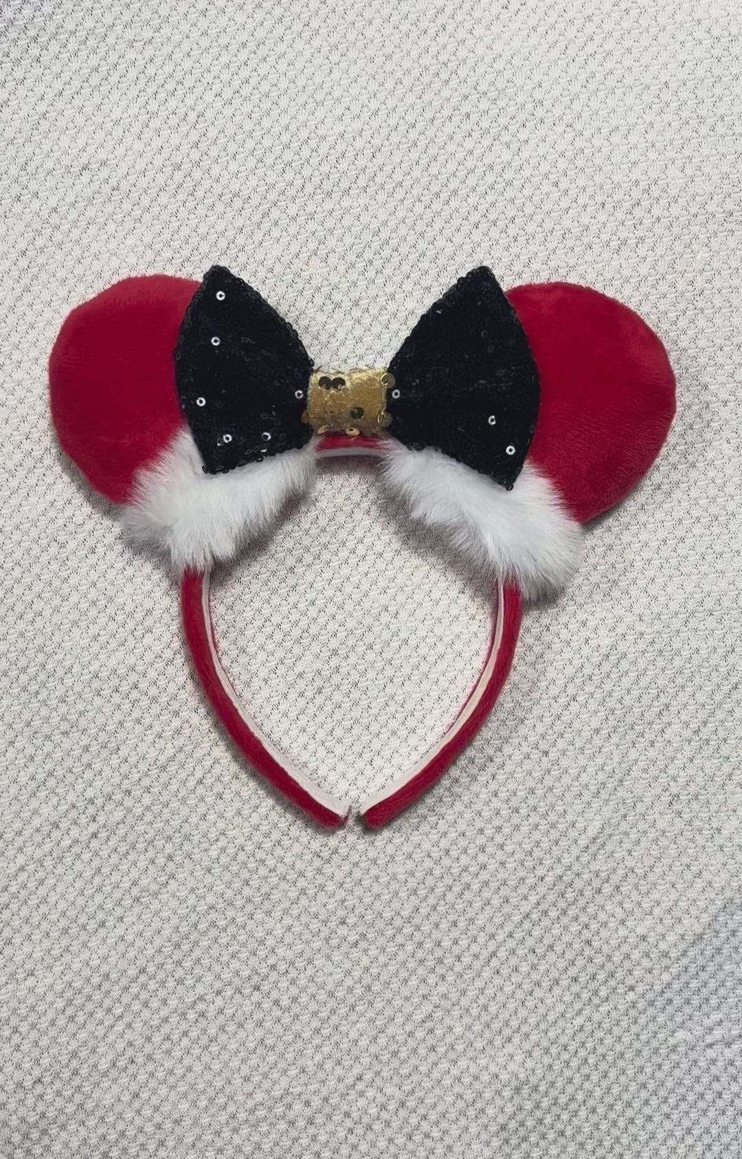 Minnie Mouse ears headband with red plush ears and black bow with gold middle and fluffy white trim on a white background