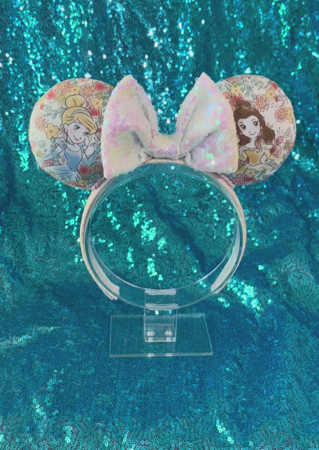 Handmade and ready to ship Pretty Princess Mouse ears with Cinderella and Belle shown on the fabric with a white iridescent bow. The headband has a white shimmery fabric and is a universal sized headband.
