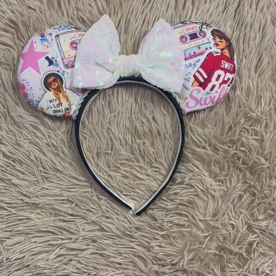 An ear headband with a large iridescent bow and custom printed ears featuring retro cassette graphics, a pink star, and a portrait of singer.