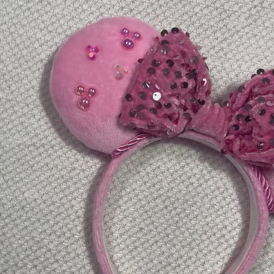 Pink mouse ears headband with decorative bow and embellishments on a gray background