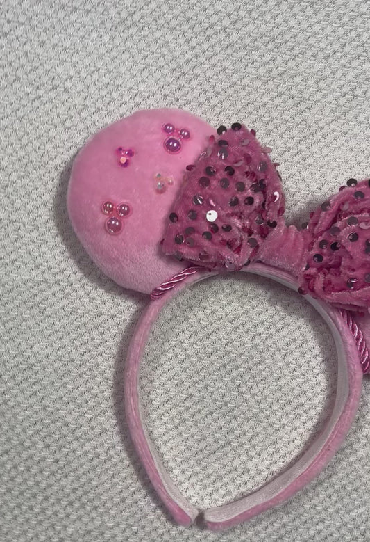 Pink mouse ears headband with decorative bow and embellishments on a gray background
