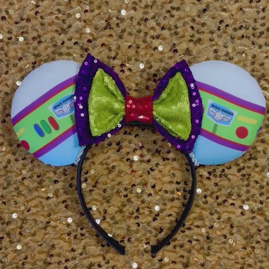 Space Ranger Mouse Ear headband with new improved bow. Handmade and ready to ship with Space ranger fabric on both the front and the back of mouse ears. The set has a silver twisted trim along the inner ears and a new sequin bow that is purple, lime green and red in sequin. Ears are on a black poly cotton universal sized headband.