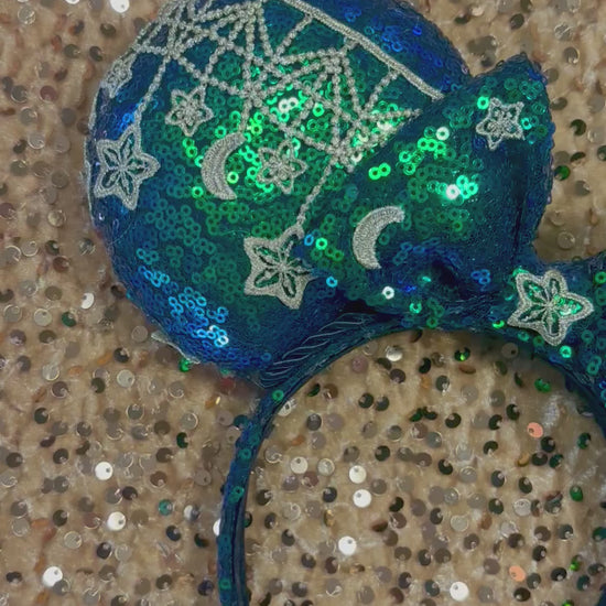 Mouse Ear headband that is a Handmade Iridescent blue and green sequins with gold sun, moon and stars attached to them. bow with star and moon patterns.