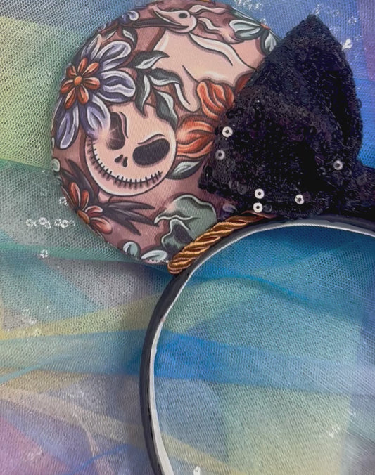 Halloween-themed NBC mouse ears on a black headband and black sequin bow and twisted trim. Shown with on a colorful background.