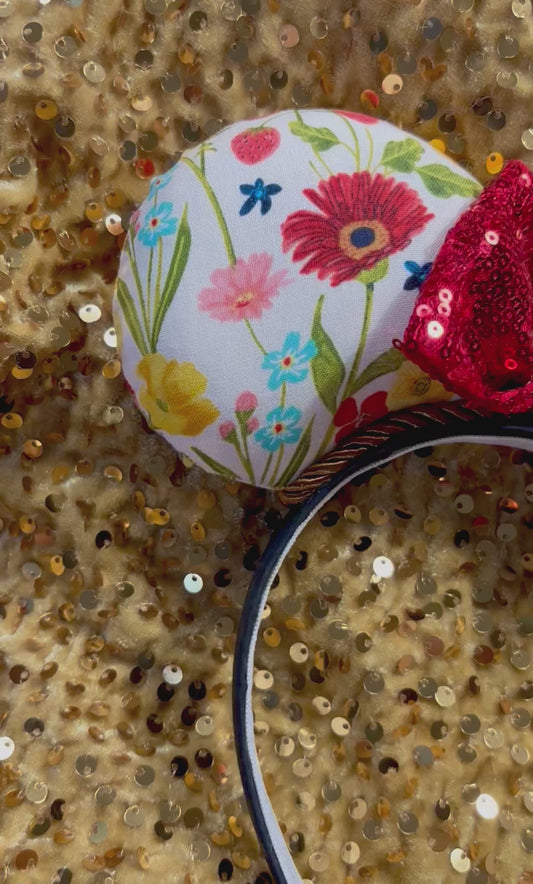 Floral-patterned mouse ears with a red bow on a gold sequin background