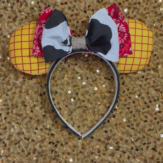 Handmade and ready to ship. Sheriff Woody Inspired mouse ears with the fabric on both the front and back that looks like his shirt. The fabric on the headband is black and is universal sized and fits most. The set has a bandana and cow print layered bow with brown trim along the inner ears to look like rope. Item is shown on a gold background.