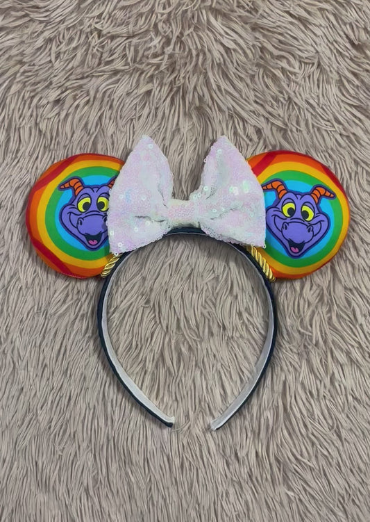 A purple dragon ear headband featuring colorful rainbow-striped ears with the Dragon and a large white iridescent bow on a black headband.