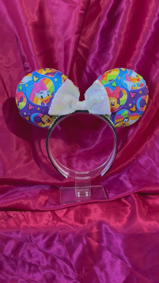 Colorful mouse ears with a white iridescent bow on a pink glittery background
