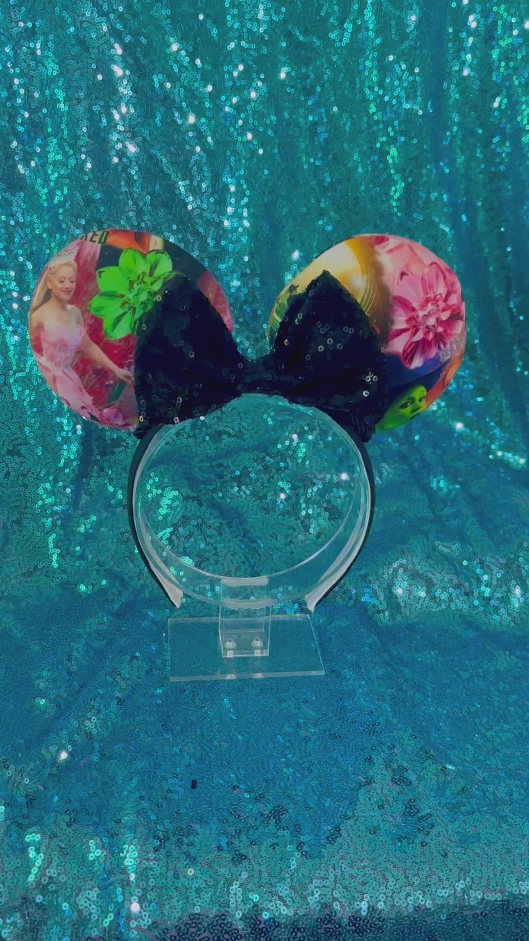 Mouse ears with floral design and black sequin bow on a blue glitter surface