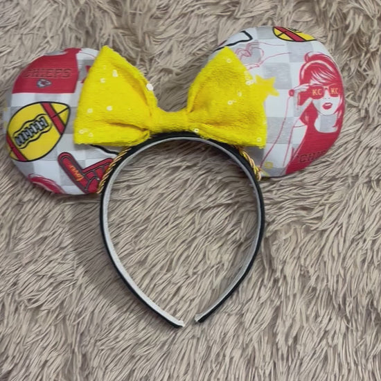 An ear headband featuring a bright yellow sequined bow. The set has TS and Chiefs images on it. Set on a universal sized headband.