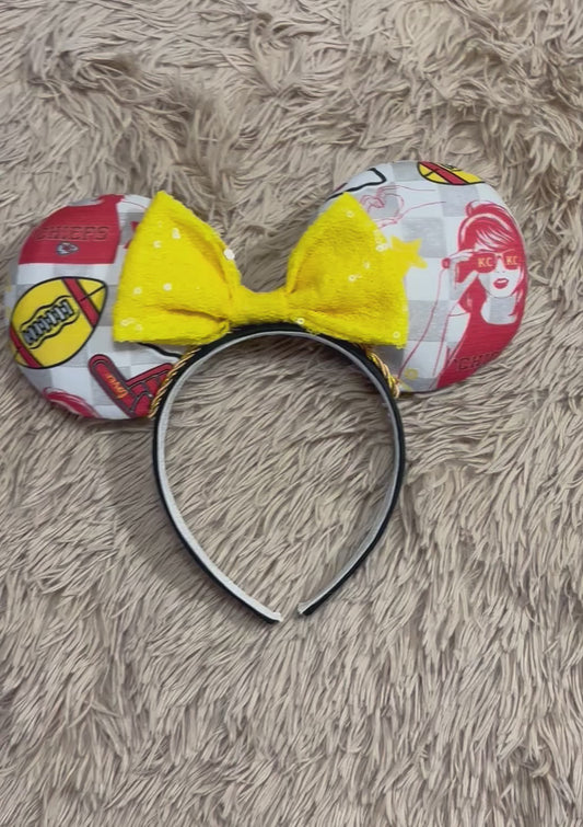 An ear headband featuring a bright yellow sequined bow. The set has TS and Chiefs images on it. Set on a universal sized headband.