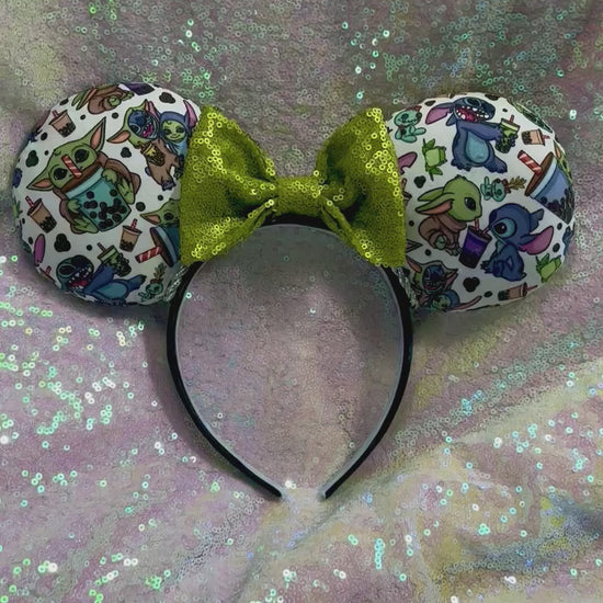 Handmade and ready to ship. Stitch and Baby Yoda are drinking coffee on the front and back with a lime green sequin bow. Shown on a white glitter background.