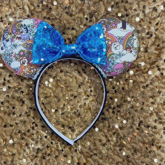 Mouse ears with a blue bow and colorful floral pattern with Bluey and friends on a gold background