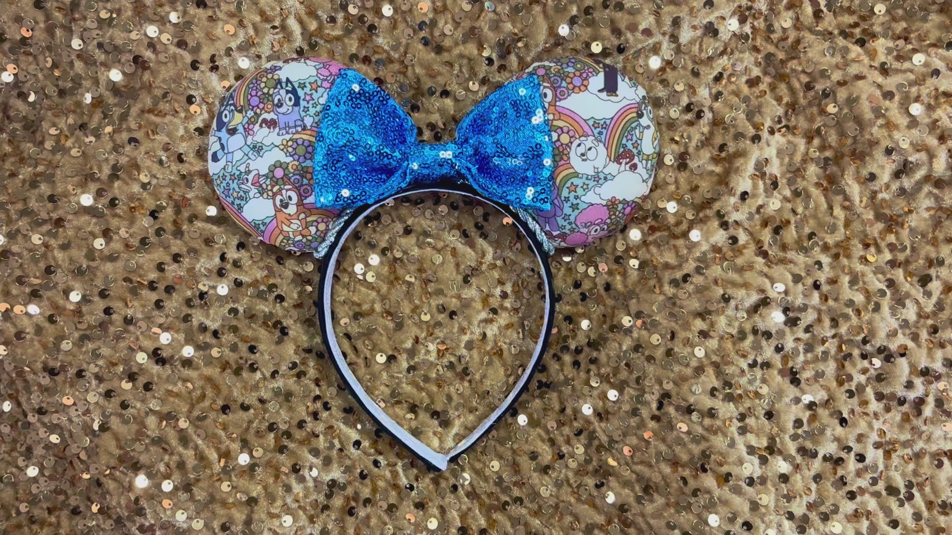 Mouse ears with a blue bow and colorful floral pattern with Bluey and friends on a gold background